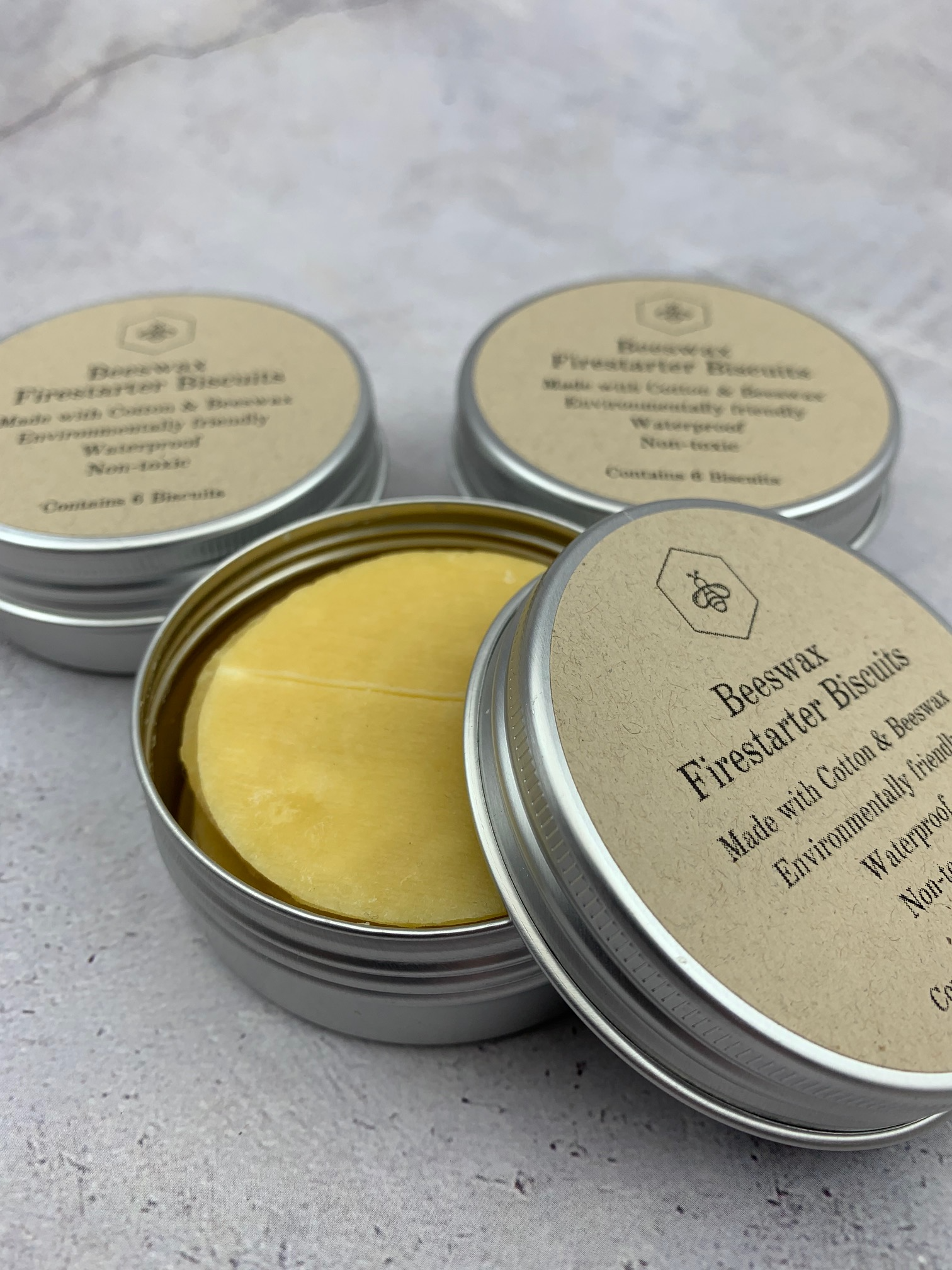 Three tins of beeswax firestarter biscuits on a light grey background. Made with Cotton & Beeswax, environmentally friendly, waterproof and non-toxic. Tin contains 6 biscuits.