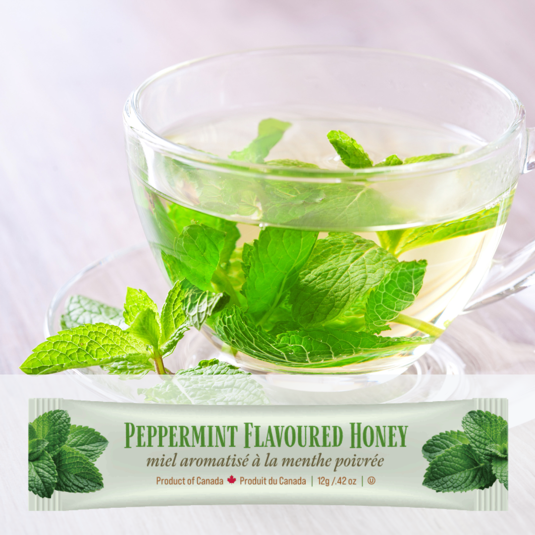 Clear glass teacup with peppermint leaves and a package of Tu-Bees peppermint-flavored honey on a white background.