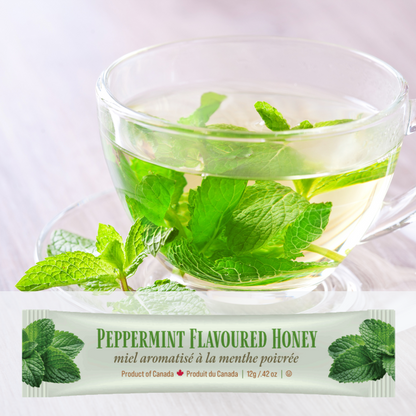 Clear glass teacup with peppermint leaves and a package of Tu-Bees peppermint-flavored honey on a white background.